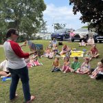 A librarian reading a story outside to a group of children and parents