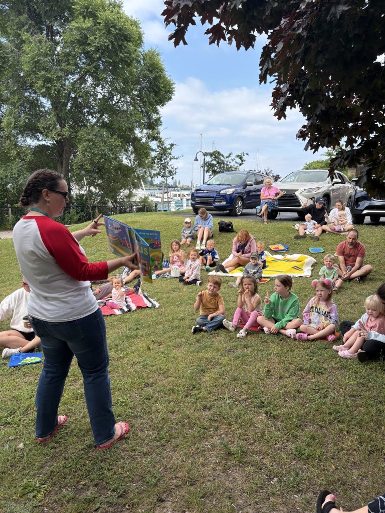 A librarian reading a story outside to a group of children and parents