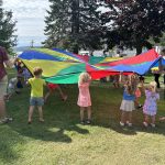 a group of children and adults playing with a parachute outside.
