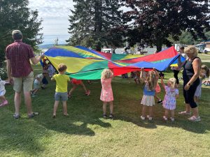a group of children and adults playing with a parachute outside.