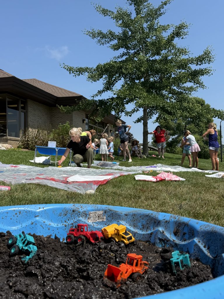kiddie pool full of mud and toy construction vehicles in front of muddy participants playing in the dirt